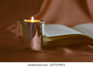 Madrid, Spain May 1, 2023 Open hardcover paper book, turning pages. Reading literature by candlelight. Burning candle in a stylish candle holder. A cozy evening at home. Knowledges, studying, read.