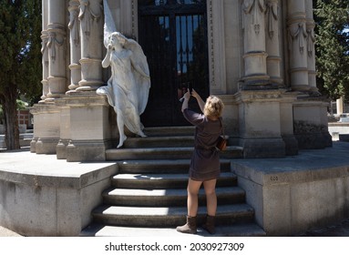 Madrid,Spain; 6th June 2021: Woman photographing the sculpture of the angel of silence by Luis Perinat at the entrance of the pantheon of the Marquise Perinat, mother of the artist.San Isidro Cemetery