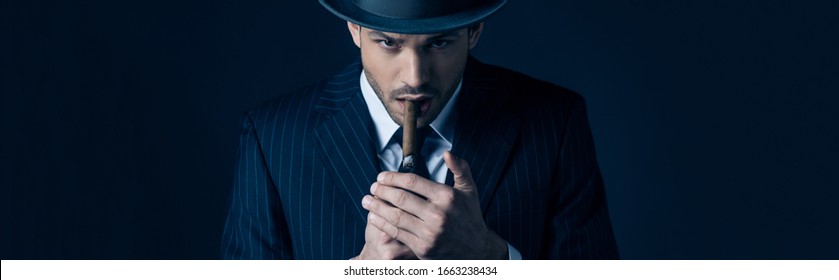 Mafioso lighting cigar and looking at camera on dark, panoramic shot