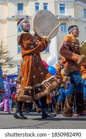 Magadan, Magadan Region, Russia - May 1, 2018. Artists In Traditional Clothes Of Indigenous Peoples Of Siberia And The Russian Far East Are Walking Along The City Street. Young Woman With A Tambourine