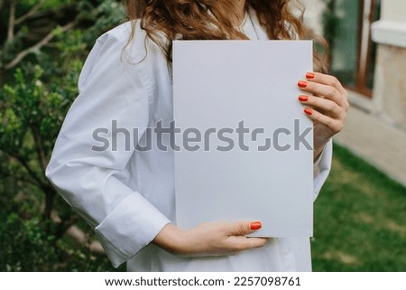 Magazine or book image mockup. Young attractive girl holding a closed book in her hands while standing in the yard.