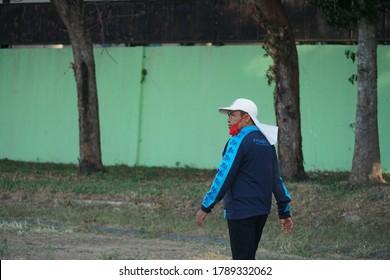 Magetan, Indonesia. July 2020: A Man Is Walking And Sporting On The Edge Of A Soccer Field Using A Red Mask And White Hat. Sports In The Covid Pandemic.