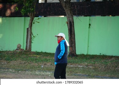 Magetan, Indonesia. July 2020: A Man Is Walking And Sporting On The Edge Of A Soccer Field Using A Red Mask And White Hat. Sports In The Covid Pandemic.