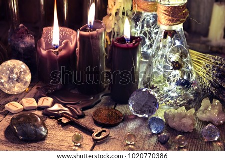 Magic crystals, ritual objects, runes, black candles and bottles on witch table. Occult, esoteric and divination concept. 
