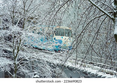 Magic fairy winter outdoor cityscape after snowfall: blue funicular in Kyiv (Kiev, Ukraine) going down the hill, snow-covered frosted branches of trees and railroads around, urban public transport 
