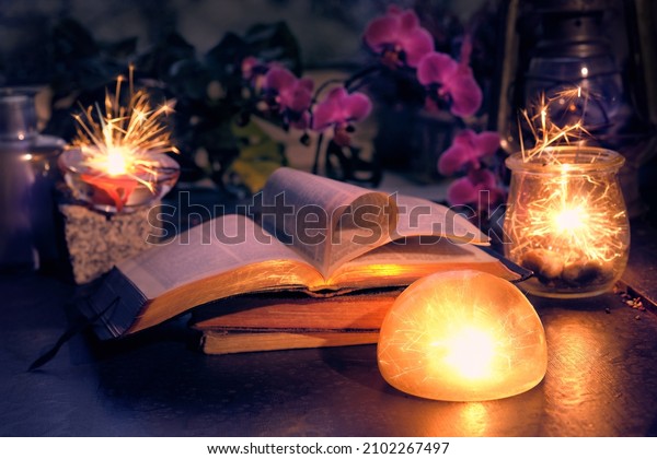 Magic lights with sparkles and orange glow in\
various glass jars. Wintertime with lights and old books. Stack of\
old vintage books with one open. Magenta orchid flowers. Romantic\
indoor background.