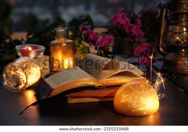 Magic lights with sparkles and orange glow in\
various glass jars. Wintertime with lights and old books. Stack of\
old vintage books with one open. Magenta orchid flowers. Romantic\
indoor background.