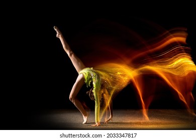 Magic of movements. Portrait of young girl, rhythmic gymnastics artist in action isolated on dark studio background with mixed light. Concept of sport, action, aspiration, beauty and motion