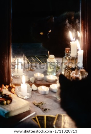 Magic and occultism concept. Reflection of a black cat, burning candles and fortune-telling cards in an old mirror