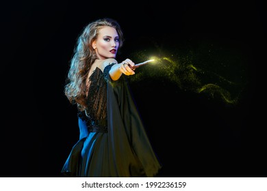 Magic on Halloween. Portrait of an enchanting young woman witch casting with a magic wand. Halloween party, make-up and costume.