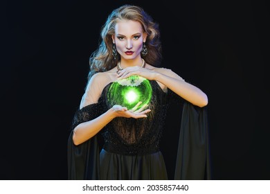 Magic on Halloween. Portrait of an enchanting young woman witch casting with an energy ball on a black background. Halloween make-up and costume.
