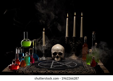 Magic potion bottles, candles and skull on the wooden table. Dark smoky background. Witchcraft, Halloween and alchemistry concept.