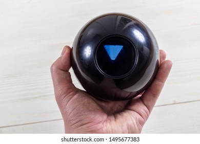 Magic prediction eight ball in hand, on the white wooden background.
