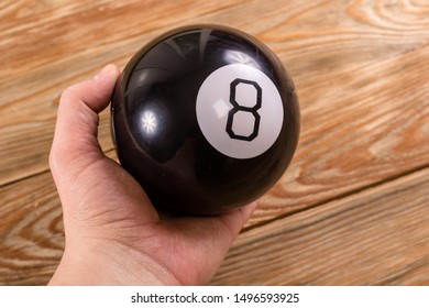 Magic prediction eight ball in hand, on the wooden background.