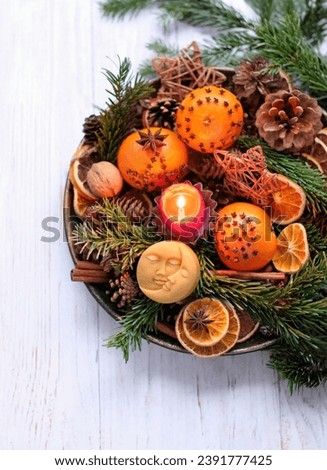 Magic Ritual for Yule sabbat. Moon amulet, candle, cinnamon, nuts, cones, decorated oranges, fir branches in plate on wooden table close up. Winter witchcraft. Festive winter season.