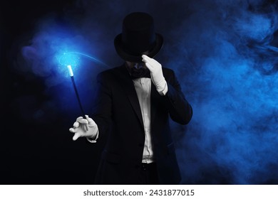 Magic and sorcery. Magician with wand and fantastic light in smoke on dark background
