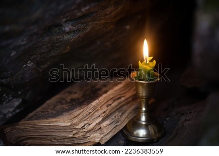 Magic theme. Burning candle and old book in stone dark niche in the forest, close up, selective focus. Foreboding, November, autumn, witchcraft, mystery, victorian style, gothic concept