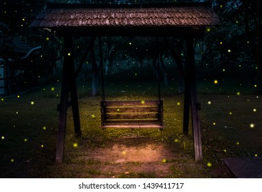 Magical Atmosphere At Night With Highlight Wooden Slider And Shining Fireflies. Fairy Tale Fantasy Scene In The Dark Forest With Lightning Bugs Flying Everywhere. The Old Charmed Slider Story For Kids