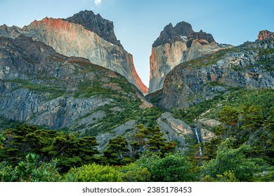 Magical colorful sunrise at major peaks, standing high towers teeth, and waterfall nearby surrounded by wet austral forests in Torres del Paine National Park, Patagonia, Chile