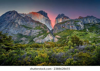 Magical colorful sunrise at major peaks, standing high towers teeth, and waterfall nearby surrounded by wet austral forests in Torres del Paine National Park, Patagonia, Chile