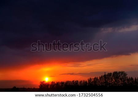 magical dramatic sunrise with tree. Dark, ominous clouds. Red, purple and blue tones