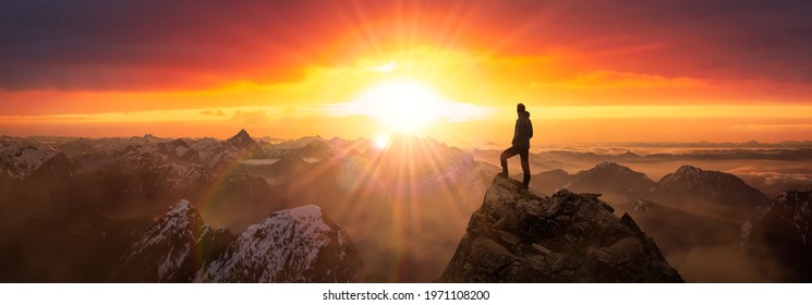 Magical Fantasy Adventure Composite Of Man Hiking On Top Of A Rocky Mountain Peak. Background Landscape From British Columbia, Canada. Sunrise Dramatic Colorful Sky