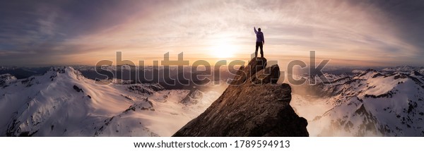 Magical Fantasy Adventure\
Composite of Man Hiking on top of a rocky mountain peak. Background\
Landscape from British Columbia, Canada. Sunset or Sunrise Colorful\
Sky