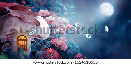 Magical fantasy elf or gnome mushroom house with window in enchanted fairy tale forest, fabulous blooming rose flower garden, flying butterflies on mysterious blue background, shine moon ray in night