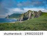 A magical green summer landscape. High steep cliffs and a blue sea. Taken from a height. Kunashir Island in the Far East. The Kurile Islands. Blooming meadows.