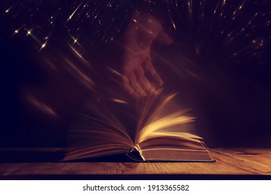 Magical image of open antique book over wooden table with glitter overlay