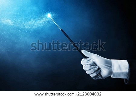 Magician hand holding magic wand on dark background