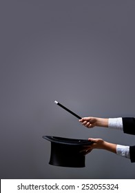 Magician hands holding hat and magic wand on gray background - with lots of copy space