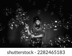 Magician lady make soap bubbles show, an illusionist in stage clothes at black background, black white image. Woman actress in theatre costume. Concept of stage perform and circus. Copy ad text space