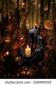 Magician Mysterious Black Cloaked Figure, Grim Reaper, Death Candlestick With Burning Candle In Dark Forest. Esoteric Spiritual Ritual For Samhain Sabbat, Halloween Holiday. Wiccan Witchcraft