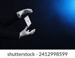 Magician showing trick with card on dark background, closeup. Space for text