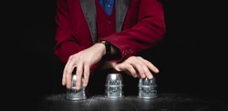 Magician Shows Shell Game Of Thimbles With Circles And Ball, Black Background. Concept Deception, Sleight Hand.