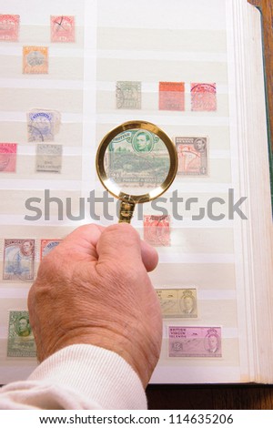 Maginfying glass held in a hand to  view stamp in a philatelic collection