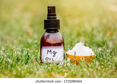 Magnesium Chloride Flakes On Brown Wooden Cup With Magnesium Vitamin Oil In Spray Bottle In Grass Outdoors With Blurred Bokeh Green Background.