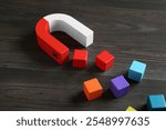 Magnet attracting with colorful cubes on wooden table, closeup