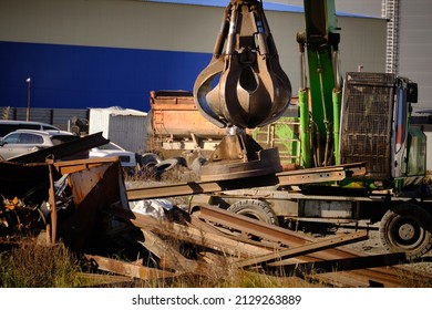 Magnet crane moves scrap metal. Hand of grabber excavator unloading recycle metal waste from truck. Clamshell at scrap metal yard
