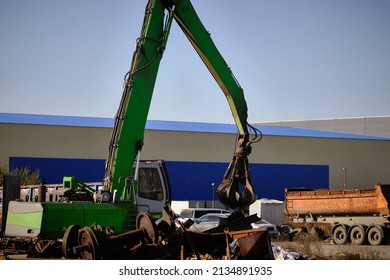 Magnet crane moves scrap metal. Hand of grabber excavator unloading recycle metal waste from truck. Clamshell at scrap metal yard