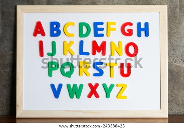 Magnet plastic alphabet on whiteboard on\
cement wall background