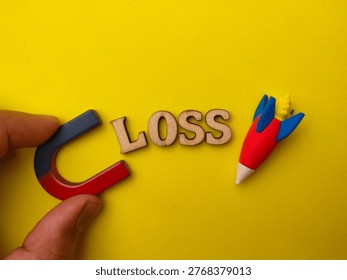 Magnet pulling a small red and blue toy rocket toward the wooden letters spelling LOSS.