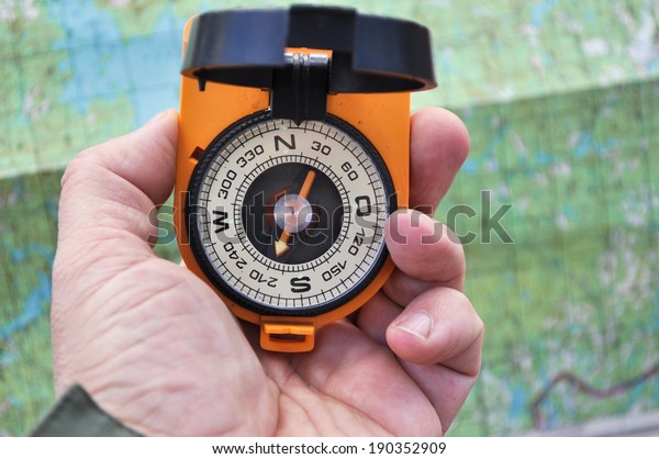 Magnetic compass in the black\
case on an orange ground with mirror cover to be in the hands of\
man.