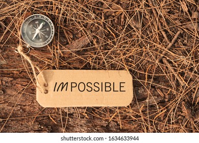 Magnetic compass and text IMPOSSIBLE or Im Possible written on paper tag at outdoor. Conceptual image with selective focus