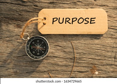 Magnetic compass and text PURPOSE written on paper tag at outdoor. Conceptual image with selective focus