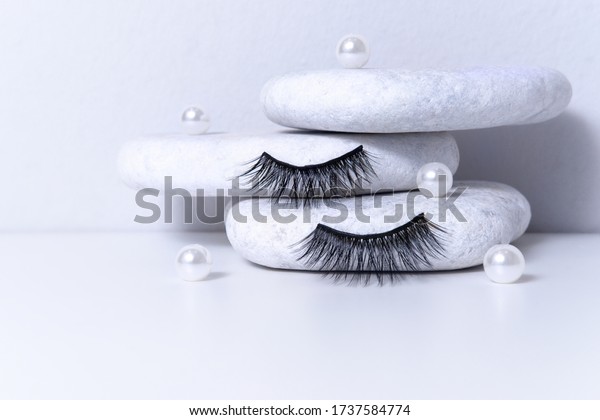 Magnetic fake artificial eyelashes\
and pearl on white stones. Home eyelash extension, cosmetology tool\
concept, beauty treatment, improving physical\
appearance