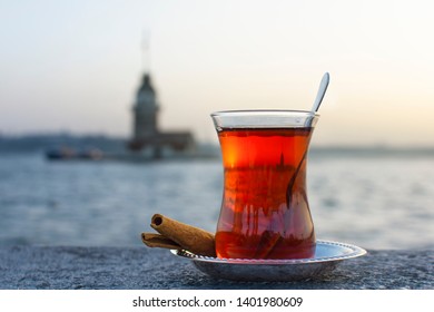 Magnific View Of Maiden's Tower (aka Kiz Kulesi) At Night Time On The Background And Traditional Turkish Tea On The Front. Istanbul Attractions.