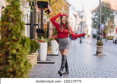 Magnificent caucasian girl in leather black shoes standing with legs crossed on pavement. Outdoor portrait of french female model in knee high boots posing in autumn day.