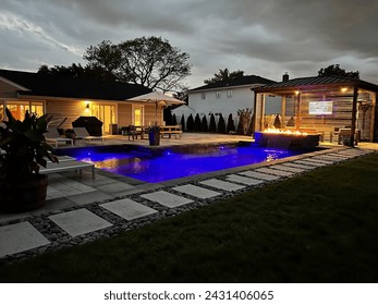 Magnificent glowing pool, cascading waterfall firepit and outdoor pavilion on a stormy summer night.  The weather does not detract from this luxurious backyard space and its modern design attributes - Powered by Shutterstock